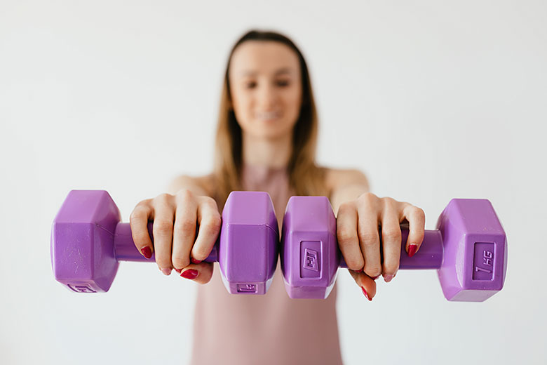 Спортивная девушка держит фиолетовые гантели перед собой